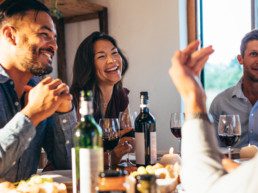 Image of friends gathering and laughing over wine and food