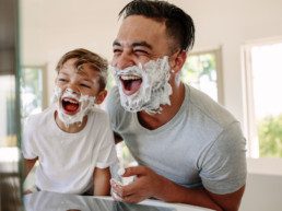 Young parent with his son, smiling and laughing in mirror. Having fun and laughing in brand new modern home for sale. They love their new home in Rosewood at Secord.